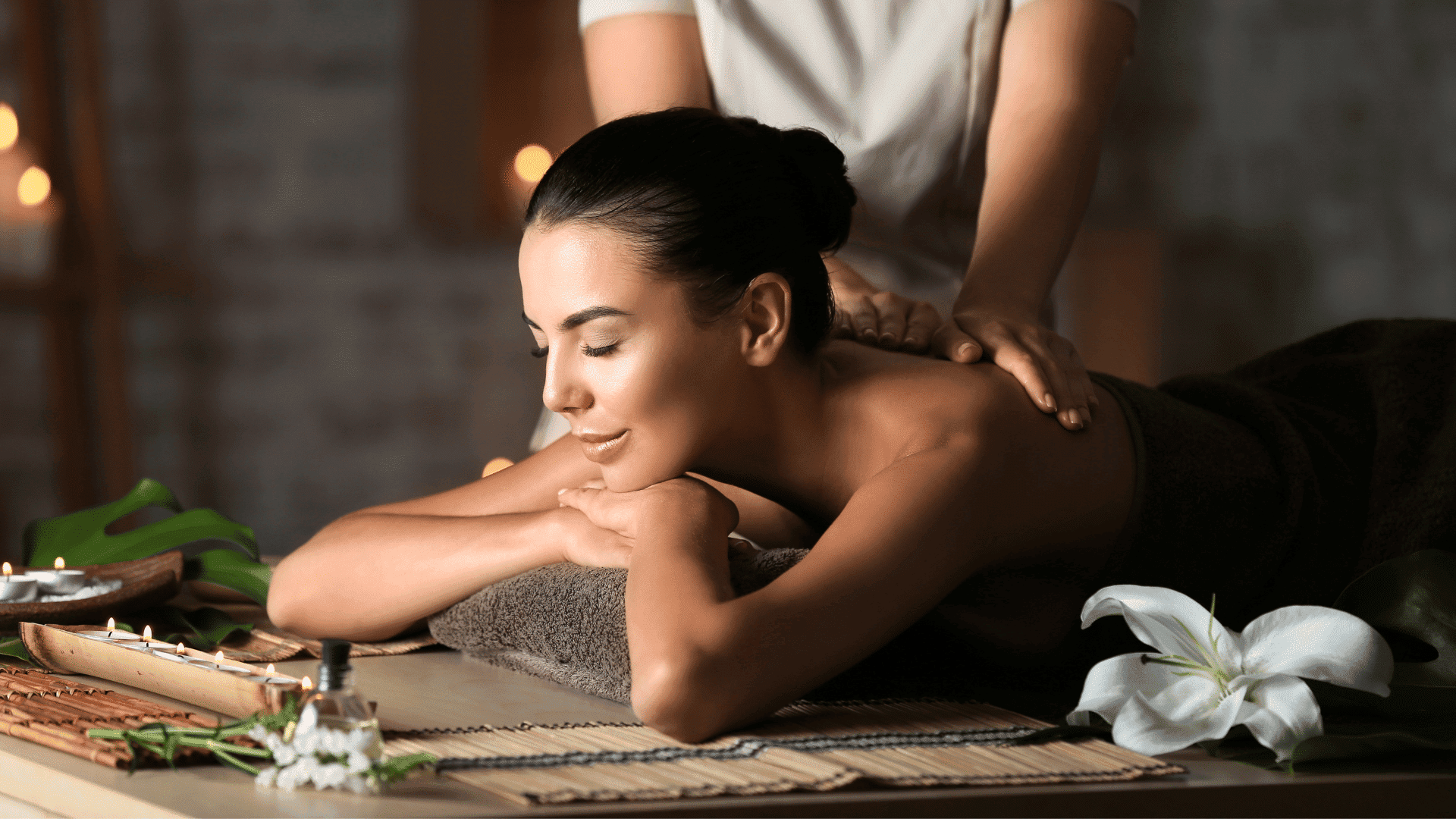 Woman receiving a relaxing massage at a spa with candles and flowers in the background.