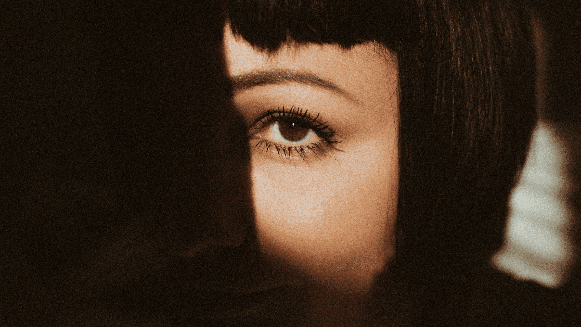 A woman's eye partially lit, with dramatic shadows highlighting her expression.