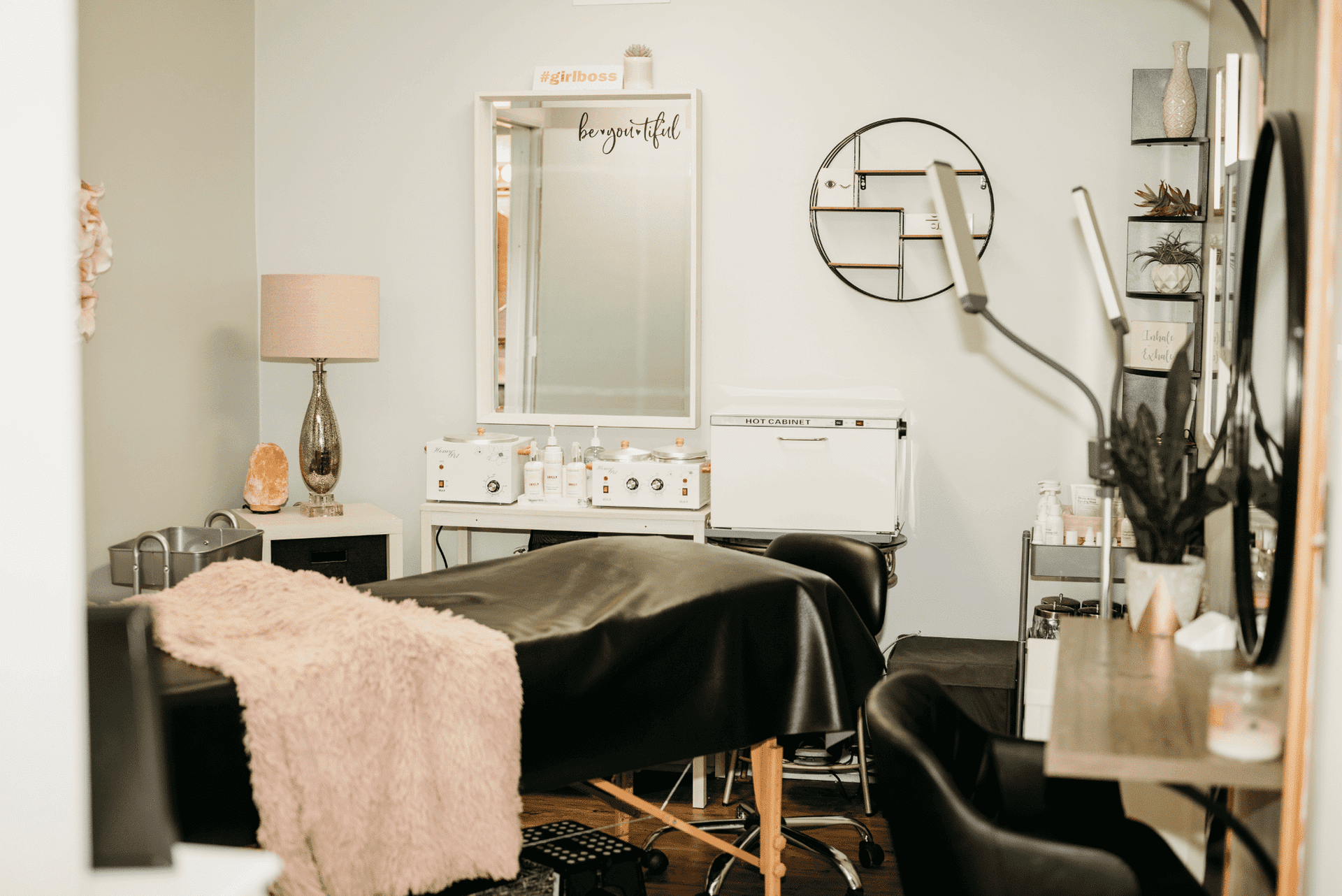 Cozy beauty salon room with treatment bed, a mirror, skincare products, and modern decor.